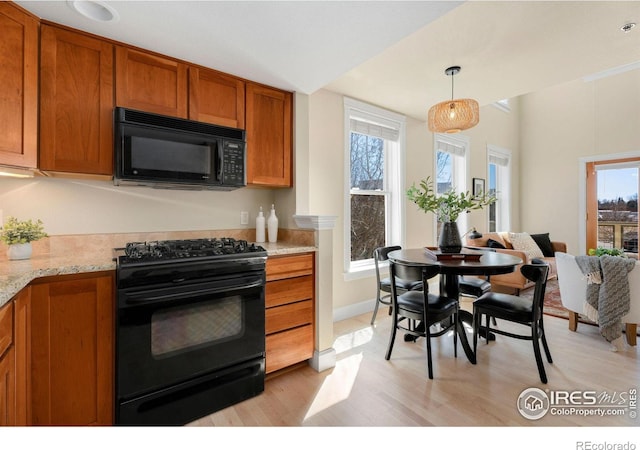 kitchen with brown cabinetry, plenty of natural light, black appliances, and decorative light fixtures