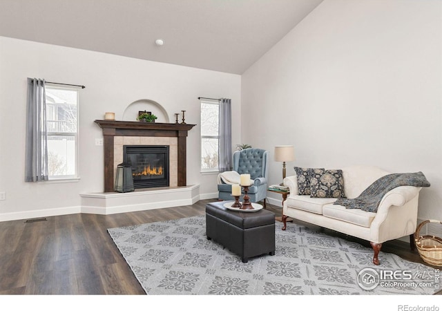 living room featuring wood finished floors, baseboards, visible vents, lofted ceiling, and a tiled fireplace