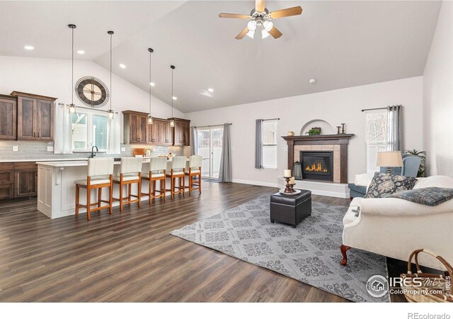 living room featuring high vaulted ceiling, a ceiling fan, dark wood finished floors, baseboards, and a tile fireplace