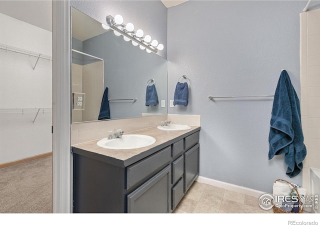 bathroom with a walk in closet, double vanity, a shower, and a sink