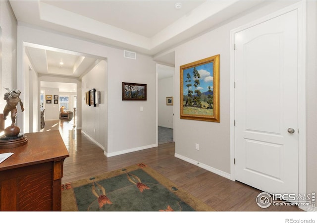 hallway featuring visible vents, a raised ceiling, baseboards, and wood finished floors
