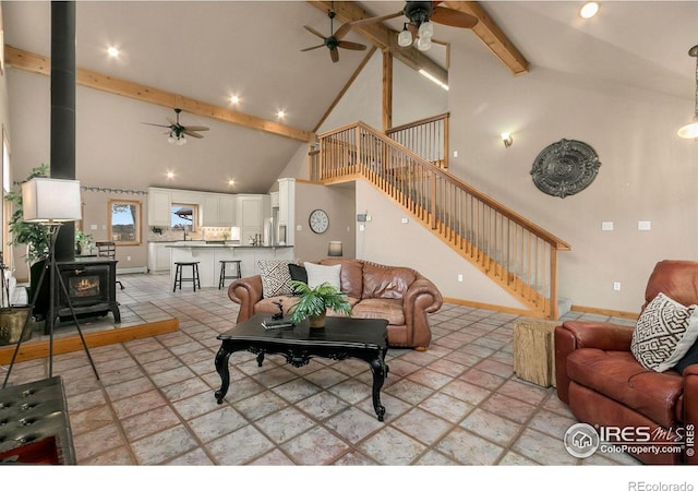 living room featuring ceiling fan, beamed ceiling, stairway, a wood stove, and high vaulted ceiling