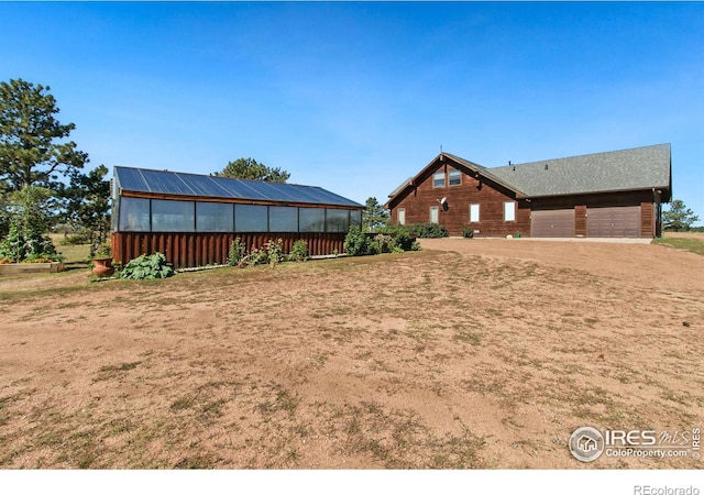 view of yard featuring a greenhouse, driveway, an outbuilding, and a garage