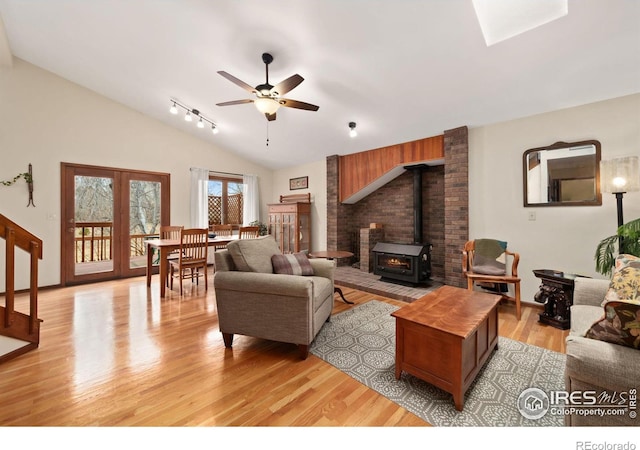 living room featuring vaulted ceiling, a wood stove, a ceiling fan, and light wood-style floors