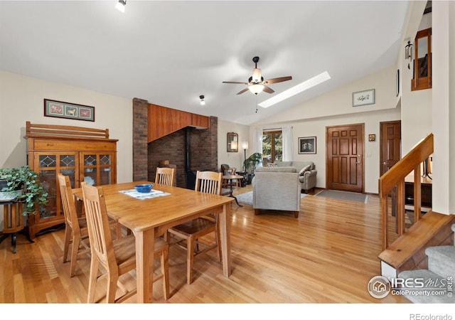 dining area featuring light wood-type flooring, lofted ceiling with skylight, a ceiling fan, and stairs