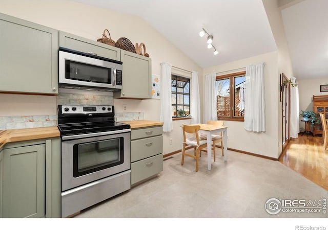 kitchen with baseboards, wooden counters, stainless steel appliances, vaulted ceiling, and green cabinets