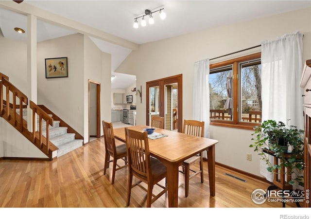 dining space featuring visible vents, stairway, light wood-style floors, and vaulted ceiling