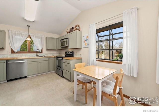 kitchen with pendant lighting, a sink, appliances with stainless steel finishes, light countertops, and vaulted ceiling