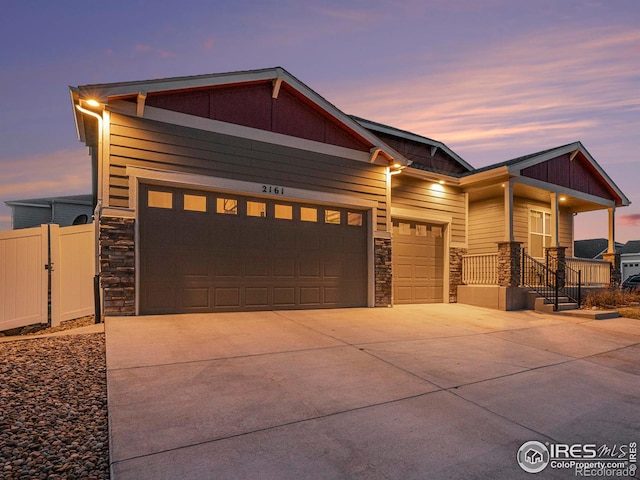 view of front of home with stone siding, concrete driveway, an attached garage, and fence