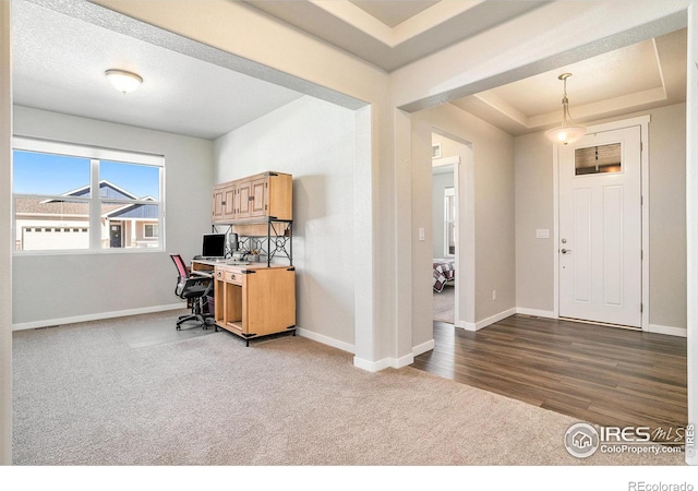 office space featuring a raised ceiling, baseboards, and dark carpet