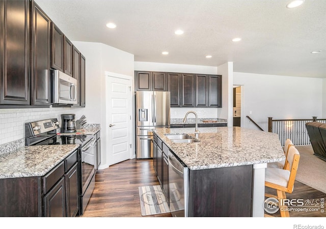 kitchen with a sink, stainless steel appliances, dark wood-type flooring, dark brown cabinetry, and a kitchen bar