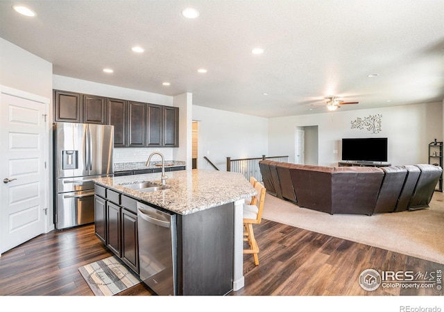 kitchen featuring open floor plan, dark wood-style floors, stainless steel appliances, a ceiling fan, and a sink