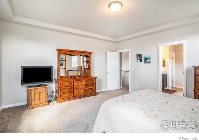 carpeted bedroom with baseboards, a raised ceiling, and ensuite bathroom