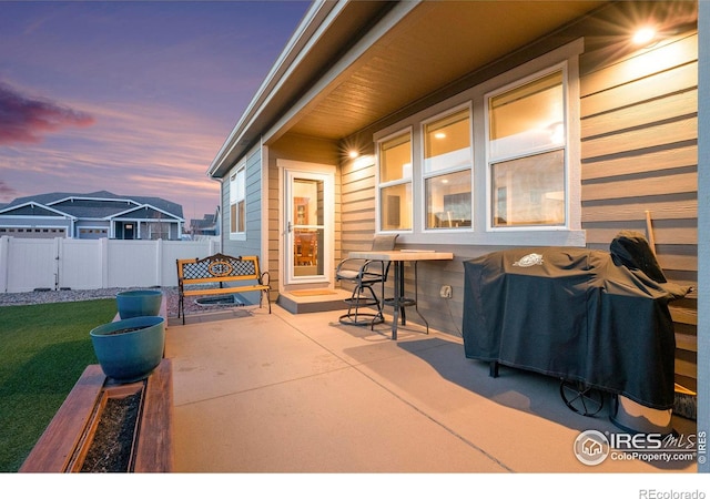 patio terrace at dusk featuring a yard, area for grilling, and fence