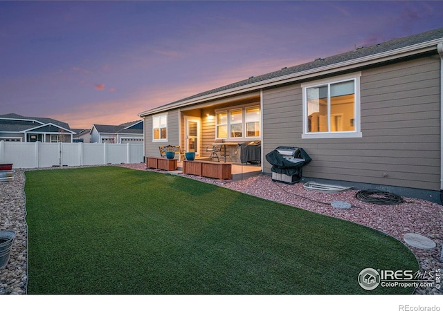 back of house at dusk with a yard, central AC, a fenced backyard, and a patio area