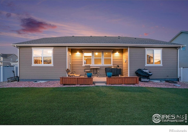 back of house at dusk with a yard and fence