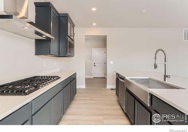 kitchen featuring a sink, stainless steel appliances, wall chimney exhaust hood, and light countertops