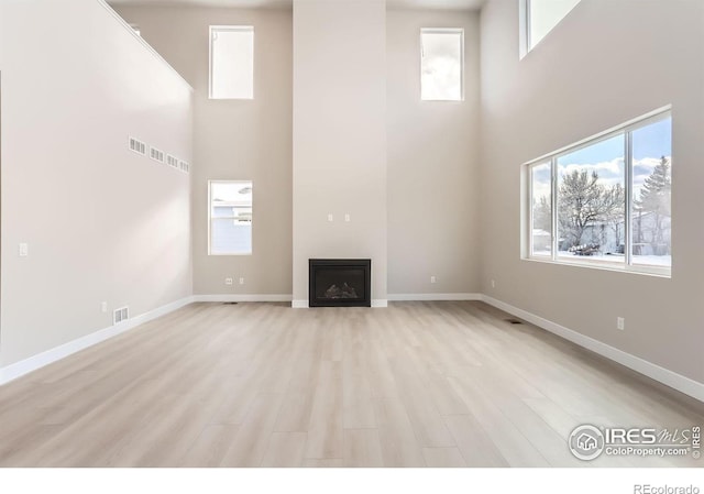 unfurnished living room with light wood finished floors, visible vents, baseboards, a fireplace, and a high ceiling