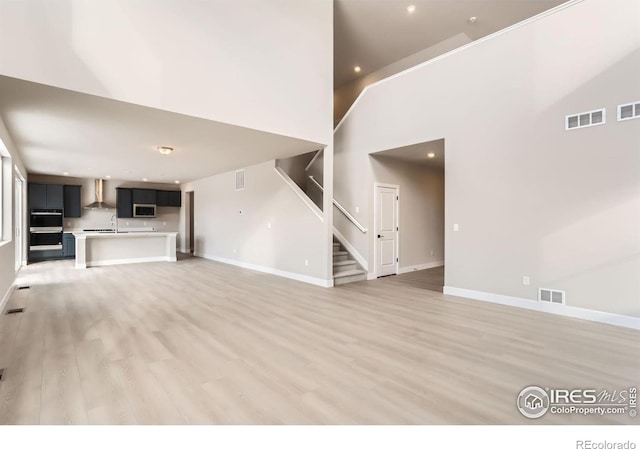 unfurnished living room with stairs, visible vents, light wood-type flooring, and baseboards