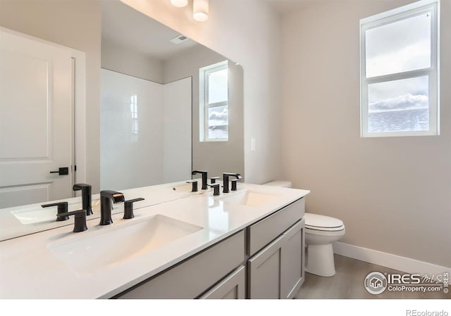 full bath with a sink, baseboards, toilet, and double vanity