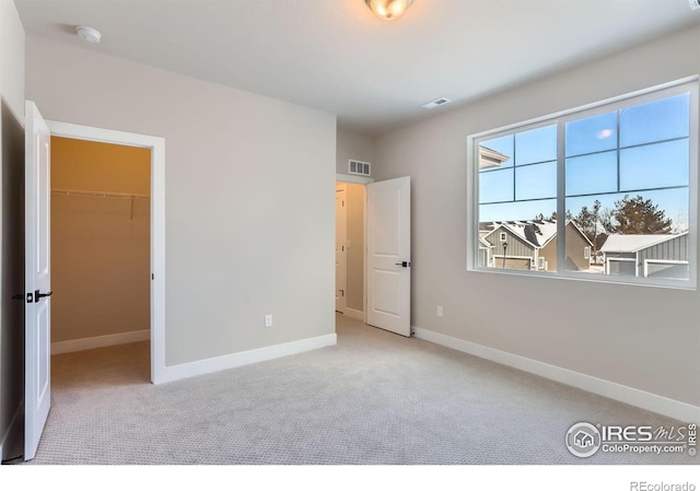 unfurnished bedroom featuring a spacious closet, carpet, visible vents, and baseboards