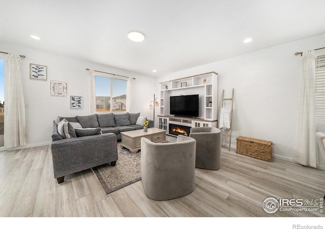 living area featuring recessed lighting, baseboards, a warm lit fireplace, and light wood-style flooring