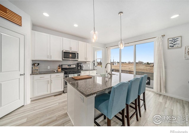 kitchen featuring a sink, backsplash, white cabinetry, appliances with stainless steel finishes, and light wood finished floors