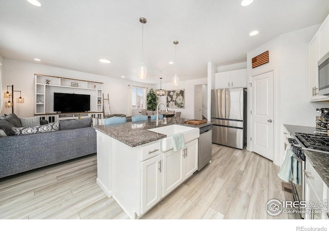 kitchen featuring light wood-type flooring, recessed lighting, dark stone countertops, stainless steel appliances, and a sink