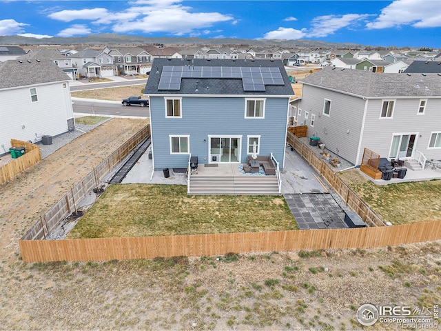 rear view of house with a fenced backyard, a yard, a residential view, solar panels, and a patio area