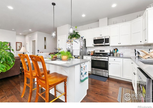 kitchen featuring backsplash, a breakfast bar area, stainless steel appliances, dark wood-style floors, and white cabinetry