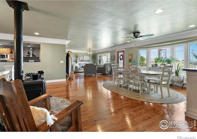 dining space with ceiling fan, a wood stove, a textured ceiling, wood finished floors, and baseboards