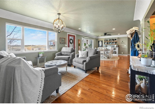 living area with recessed lighting, ceiling fan with notable chandelier, a textured ceiling, and wood finished floors
