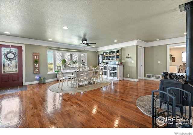 dining area with baseboards, a wood stove, visible vents, ceiling fan, and wood finished floors