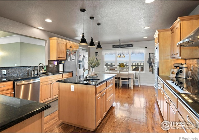 kitchen with a center island with sink, a sink, wall chimney range hood, and stainless steel appliances