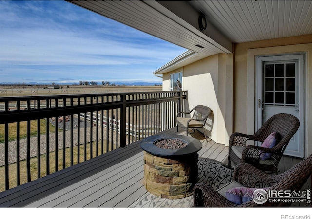 wooden deck with a rural view and a fire pit