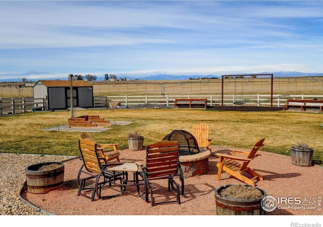 view of patio / terrace with a rural view, fence, a fire pit, and an outdoor structure