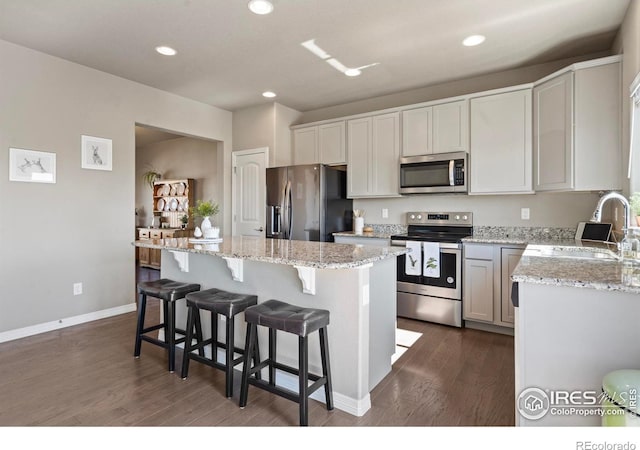 kitchen with stainless steel appliances, a sink, a center island, dark wood-type flooring, and light stone counters