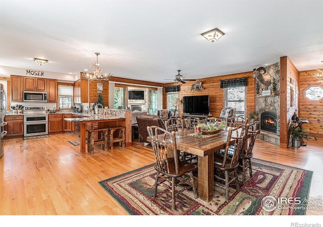 9512 County Road 43, Glen Haven, CO 80532 - dining area with light wood-style floors, wood walls, a fireplace, and ceiling fan with notable chandelier