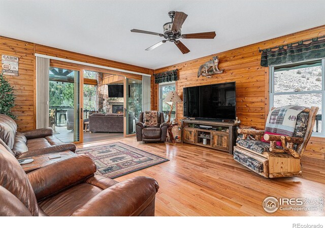 9512 County Road 43, Glen Haven, CO 80532 - living room featuring a lit fireplace, wood finished floors, a ceiling fan, and wood walls