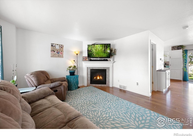 living room featuring a fireplace, wood finished floors, visible vents, and baseboards