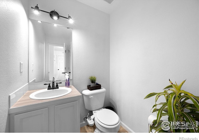 half bath with baseboards, toilet, vanity, and a textured wall