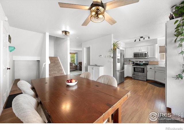dining room with track lighting, a ceiling fan, wood finished floors, and stairs