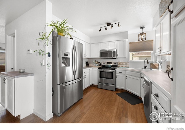 kitchen with dark wood finished floors, a sink, white cabinets, appliances with stainless steel finishes, and decorative light fixtures