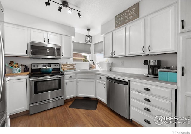 kitchen with wood finished floors, appliances with stainless steel finishes, white cabinetry, and a sink