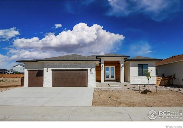 prairie-style house with a garage, stone siding, concrete driveway, french doors, and stucco siding