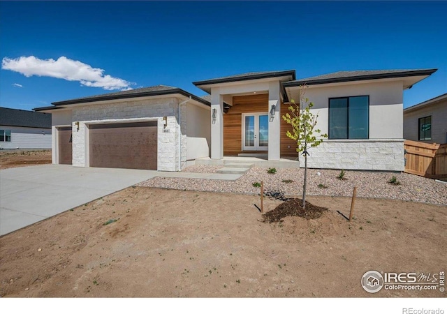 prairie-style home featuring french doors, stone siding, a garage, concrete driveway, and stucco siding