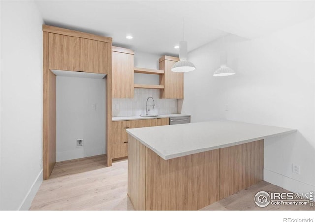 kitchen with a sink, a peninsula, light countertops, light wood-style floors, and tasteful backsplash
