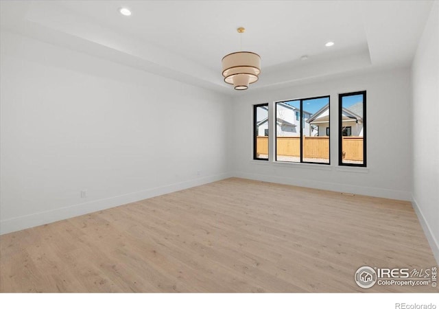 unfurnished room featuring a raised ceiling, wood finished floors, baseboards, and recessed lighting