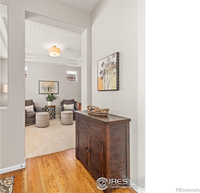 hallway with light carpet, light wood-type flooring, and baseboards