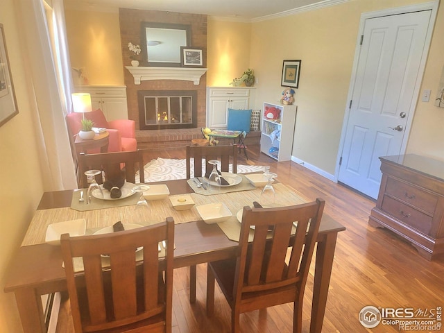 dining room featuring a brick fireplace, crown molding, baseboards, and wood finished floors